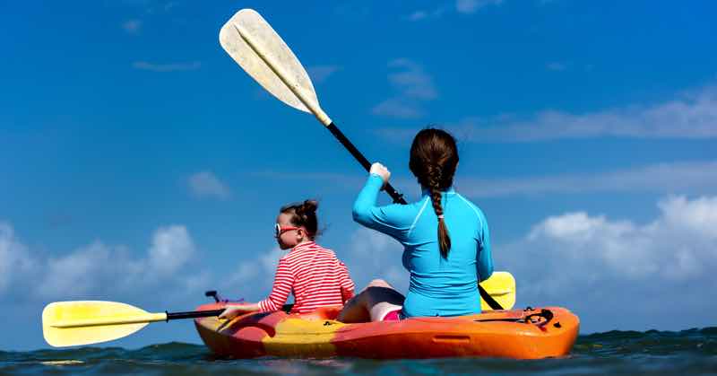Family of mother and daughter paddling on kayaks at tropical ocean water during summer vacation